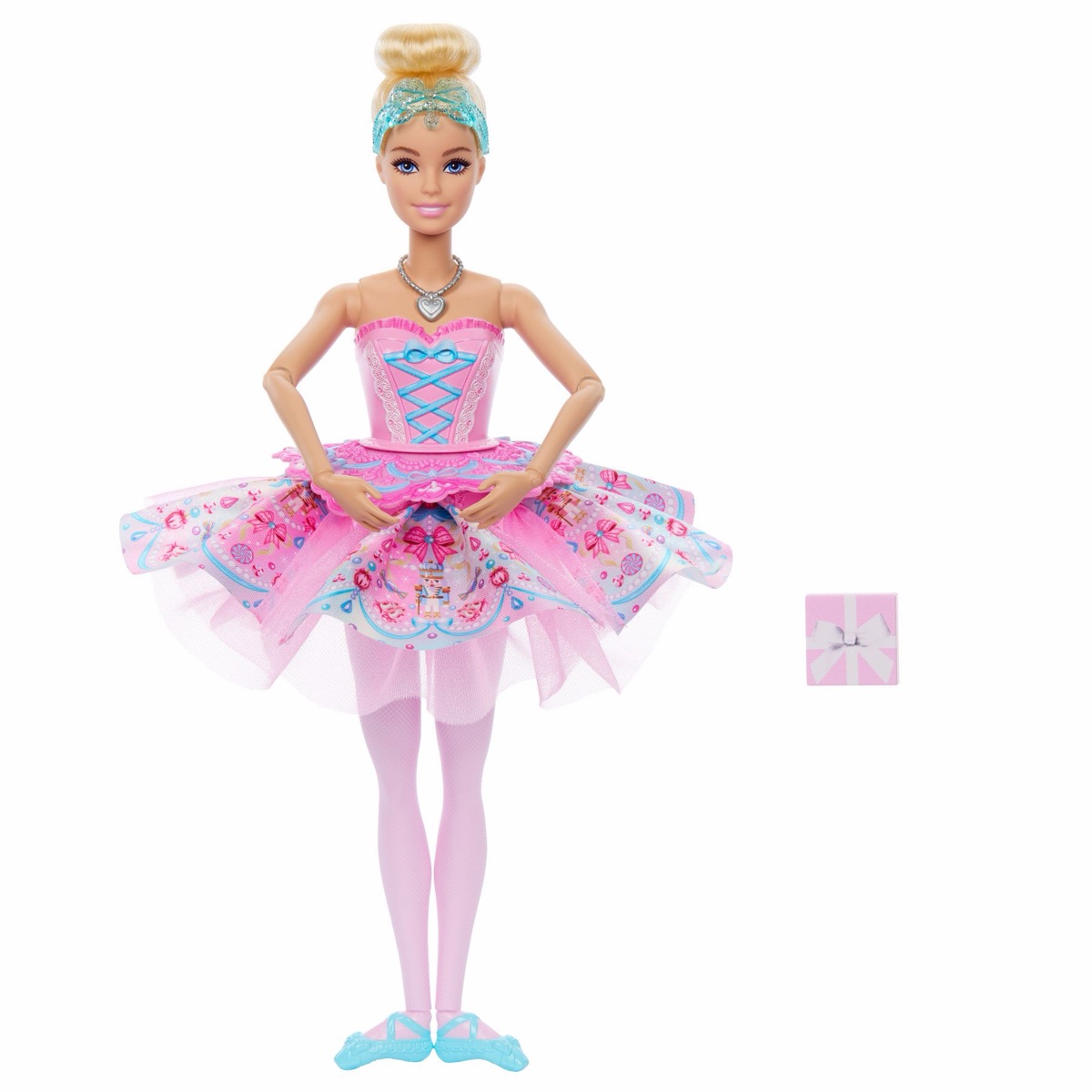 Mattel-Pressebild: Clara-Deluxe-Puppe JLW53 mit blondem Dutt, rosa Ballettkleid mit Süßigkeiten-Muster und hellblauen Ballettschuhen, daneben ein kleines Geschenkpäckchen