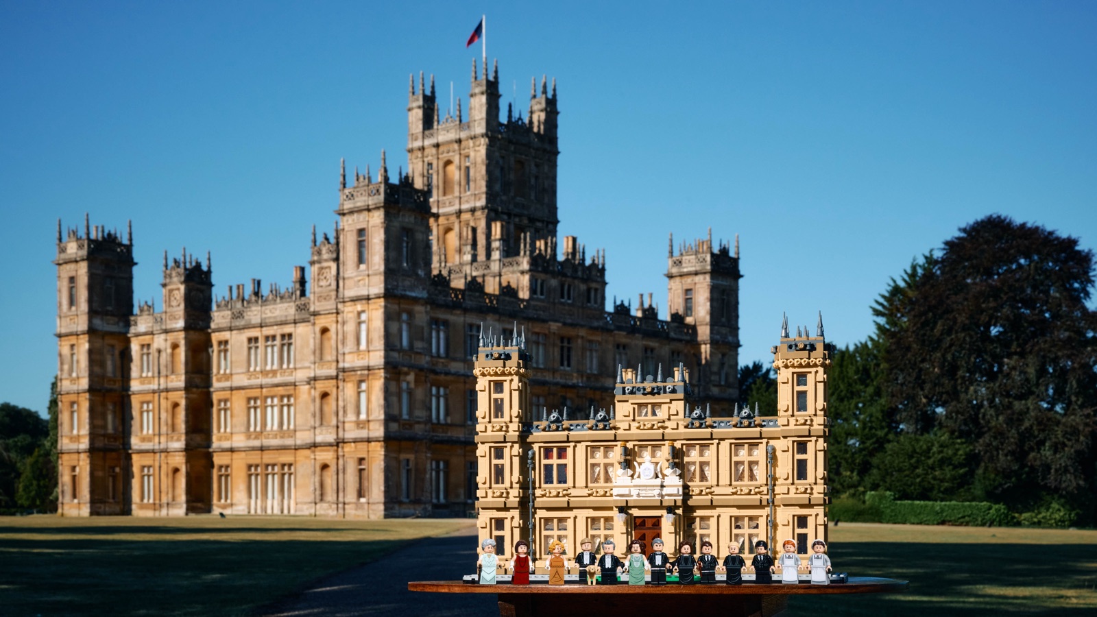 Das LEGO Modell Downton Abbey 21373 mit 13 Minifiguren auf einem Tisch vor dem echten Highclere Castle