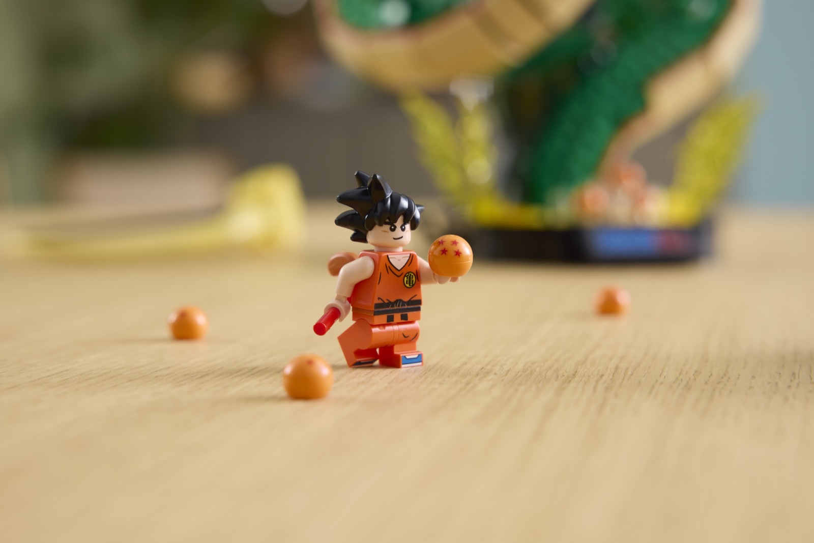 Die LEGO Minifigur des jungen Goku im orangefarbenen Anzug mit rotem Kampfstab hält eine Dragon Ball mit roten Sternen, um ihn herum liegen weitere Kugeln auf einem Holztisch