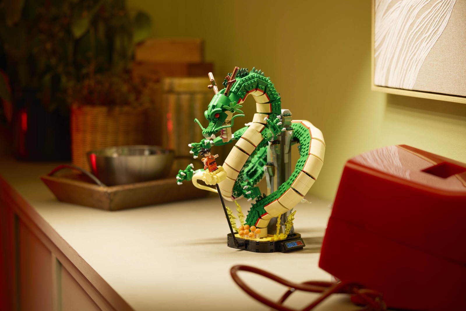 Der grüne LEGO-Drache Shenron windet sich auf einer Anrichte um eine graue Säule nach oben, vorn links der junge Goku auf seiner Wolke, am Sockel die orangefarbenen Dragon Balls