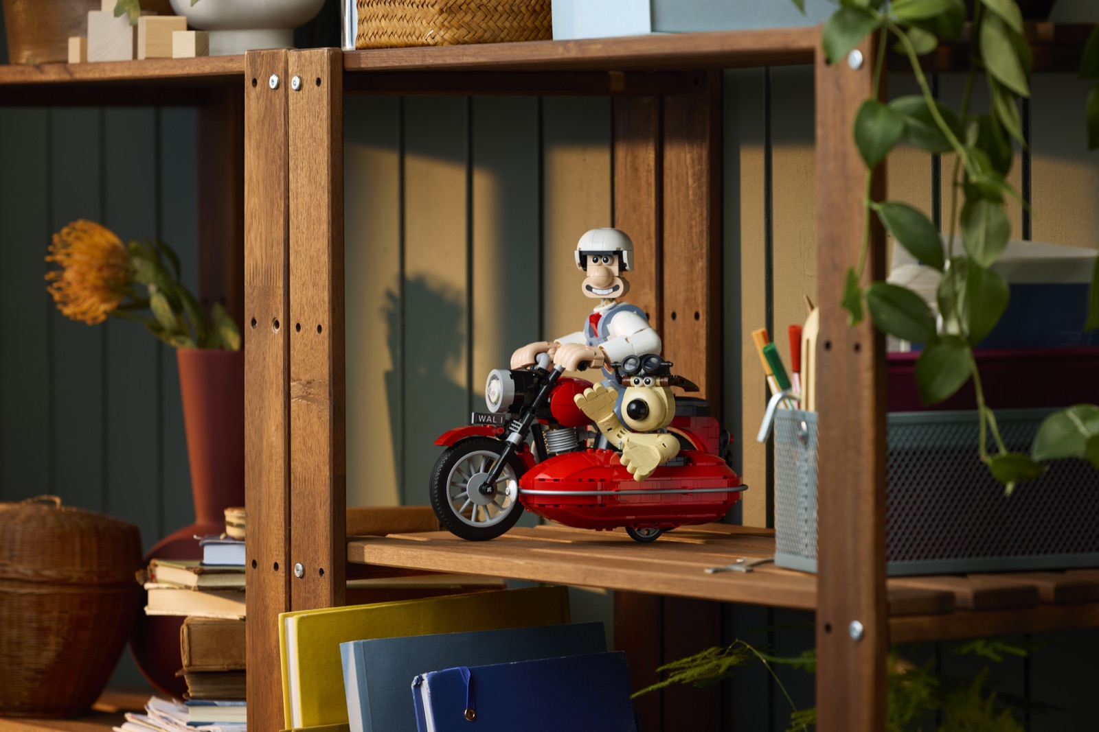 Wallace mit Helm auf dem roten LEGO-Motorrad, Gromit im Beiwagen, aufgestellt in einem Holzregal