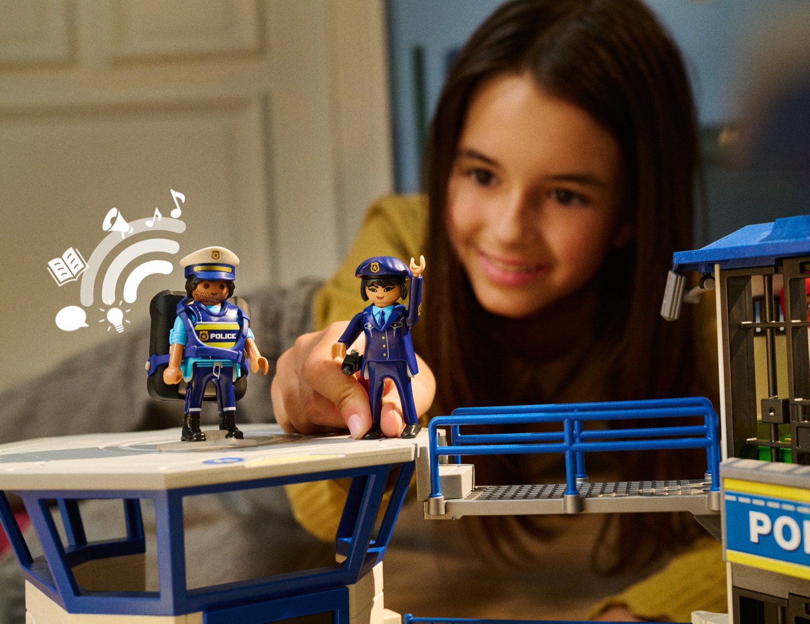 Ein Mädchen spielt mit zwei Playmobil-Polizeifiguren vor der Polizei-Kommandozentrale, eine Figur trägt den Audio-Rucksack