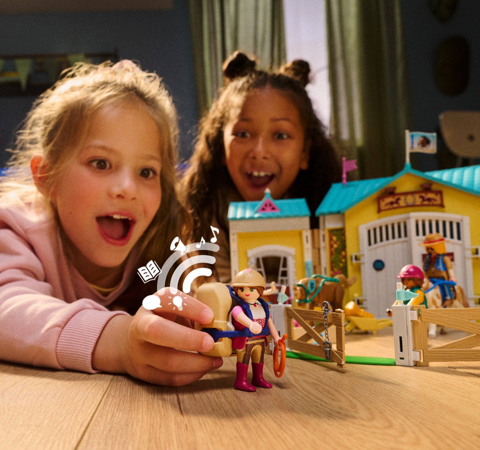 Zwei Mädchen schauen gespannt auf eine Playmobil-Reiterin mit Audio-Rucksack vor dem Reiterhof